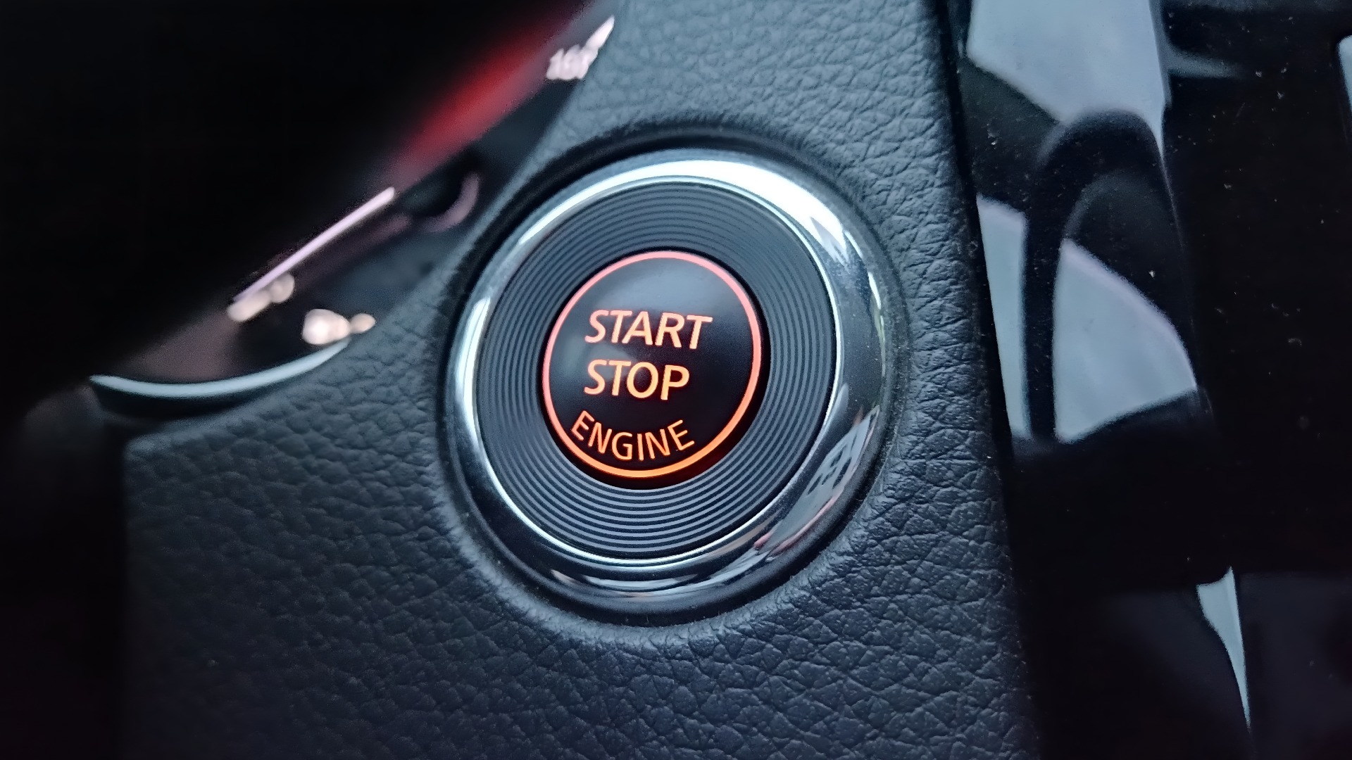 Nahaufnahme eines beleuchteten Start-Stopp-Knopfes auf dem Armaturenbrett eines modernen Fahrzeugs. Konzept für ein schlüsselloses Zugangssystem und ein Zündsteuerungssystem. Startknopf für den Fahrzeugmotor.